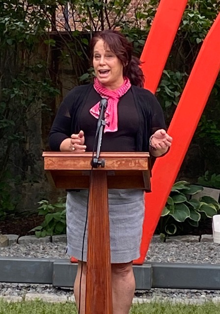 a woman standing at a podium in front of a red sculpture.