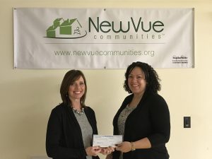 2 smiling women hold a check while standing in front of a NewVue Communities banner on the wall
