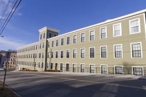 a large horizontal building with olive sides and rectangle windows, with a road in the foreground
