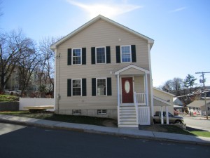 a house with white siding, red front door, and white front steps, with a hilly street visible in front