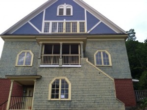 an upside down photo of a house exterior with weathered siding, windows, and upper balcony, with blue paint on the top floor