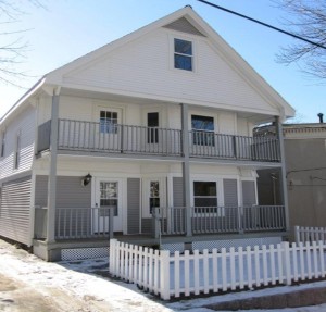 a 2 floor multi unit house with gray and white siding, white doors, and gray porch railings