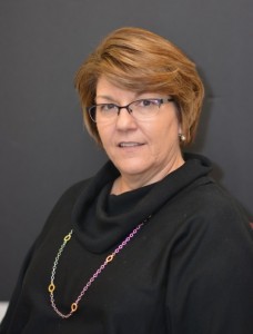 a portrait photo of a woman with short brown hair, dark glasses, a black collared sweater and a colorful necklace chain