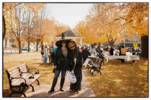 2 adults in Halloween costumes, a witch and a pumpkin-head, pose outdoors for the camera on a sunny day