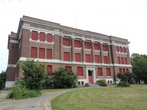 a large brick building with the windows and front door covered with red painted wood