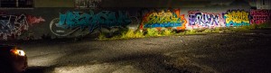 a concrete wall with colorful graffiti, illuminated by car headlights