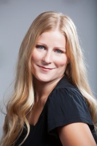 a portrait photo of a gently smiling blond woman in a black shirt