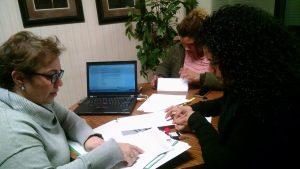 3 women at a table discussing paperwork, with a laptop open to a text document