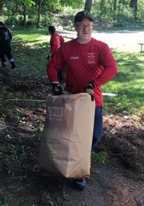 a man in a red long sleeve shirt stands outside holding a large paper leaf bag