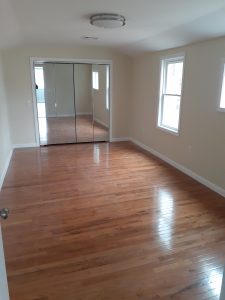 an empty room with wood flooring, beige walls, and mirrored closet doors