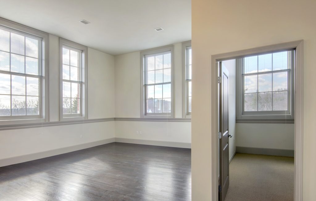 an empty room with open windows letting in daylight, with an open doorway to another empty room
