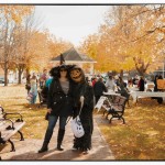 2 adults in Halloween costumes, a witch and a pumpkin-head, pose outdoors for the camera on a sunny day