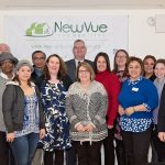 a group of smiling people stand in front of a NewVue Communities banner on the wall