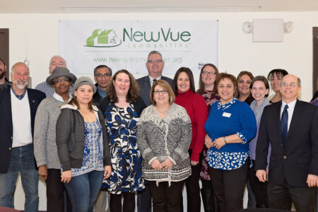 a group of smiling people stand in front of a NewVue Communities banner on the wall