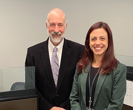 a man in a black suit and a woman in a green blazer smile at the camera