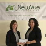 2 smiling women hold a check while standing in front of a NewVue Communities banner on the wall