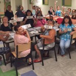 people seated at tables arranged in a square, holding up printed fake 100 dollar bills